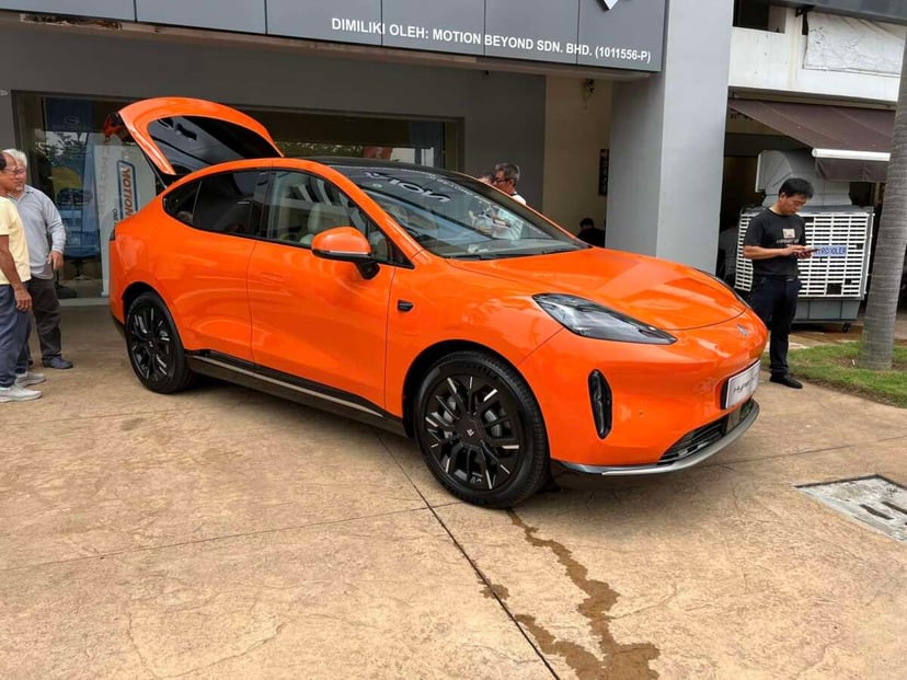 right orange GAC Aion Hyptec HT electric vehicle with black alloy wheels on display outside a showroom. The car's gullwing doors are open, showcasing its sleek, aerodynamic design. Several people are standing nearby, examining the vehicle